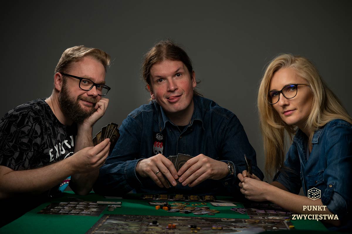 trzy osoby siedzą przy stoliku do gier i grają w planszówki